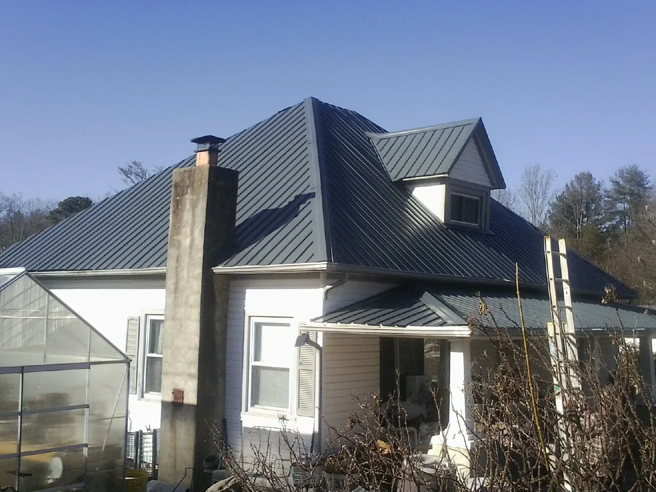 Dark blue standing seam metal roof on a white farmhouse with dormer — Slate & Tile Roof Repair by Roofing Brothers in Highland Lakes