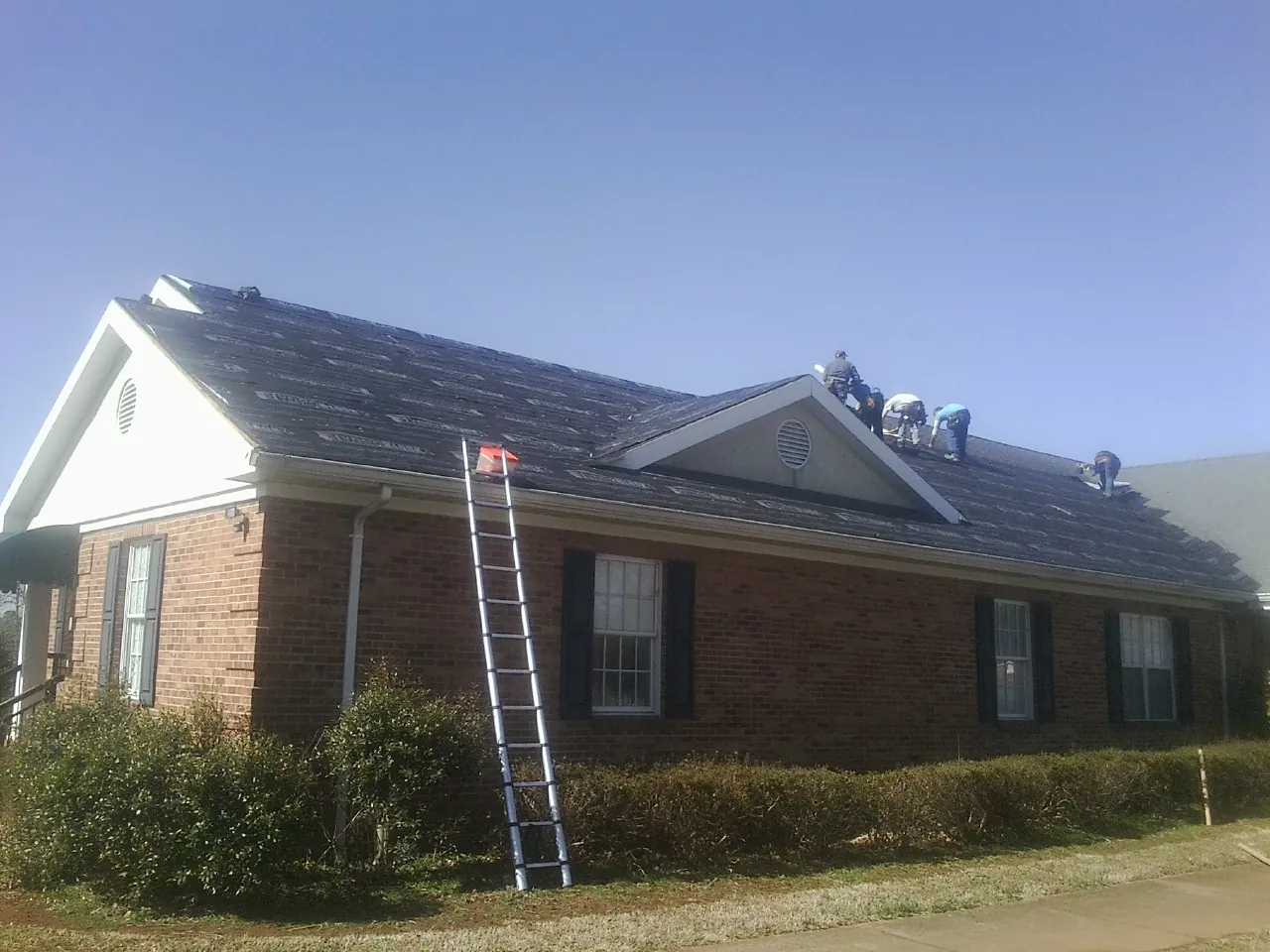 Crew tearing shingles off a brick ranch roof with a ladder set — Metal Roof Repair work by our crew in Highland Lakes