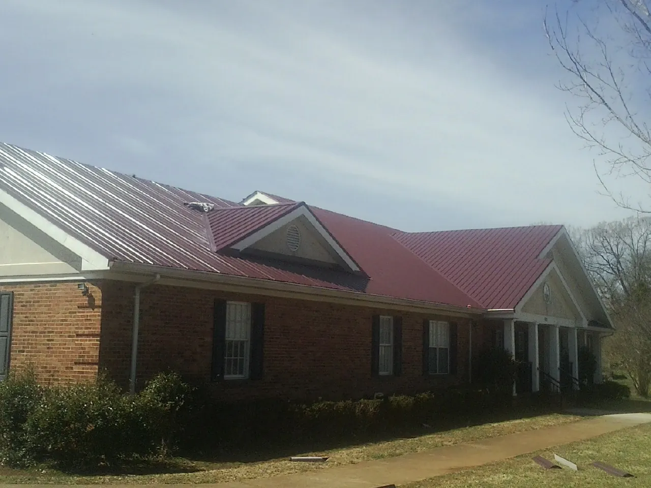 Red metal roof with gabled entries on a long brick building, from a Hail Damage Roof Repair job in Highland Lakes