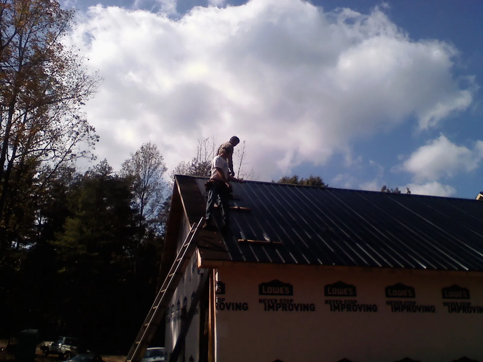 Roofer fastening dark metal panels high against a cloudy sky, from a Roof Inspection job in Highland Lakes