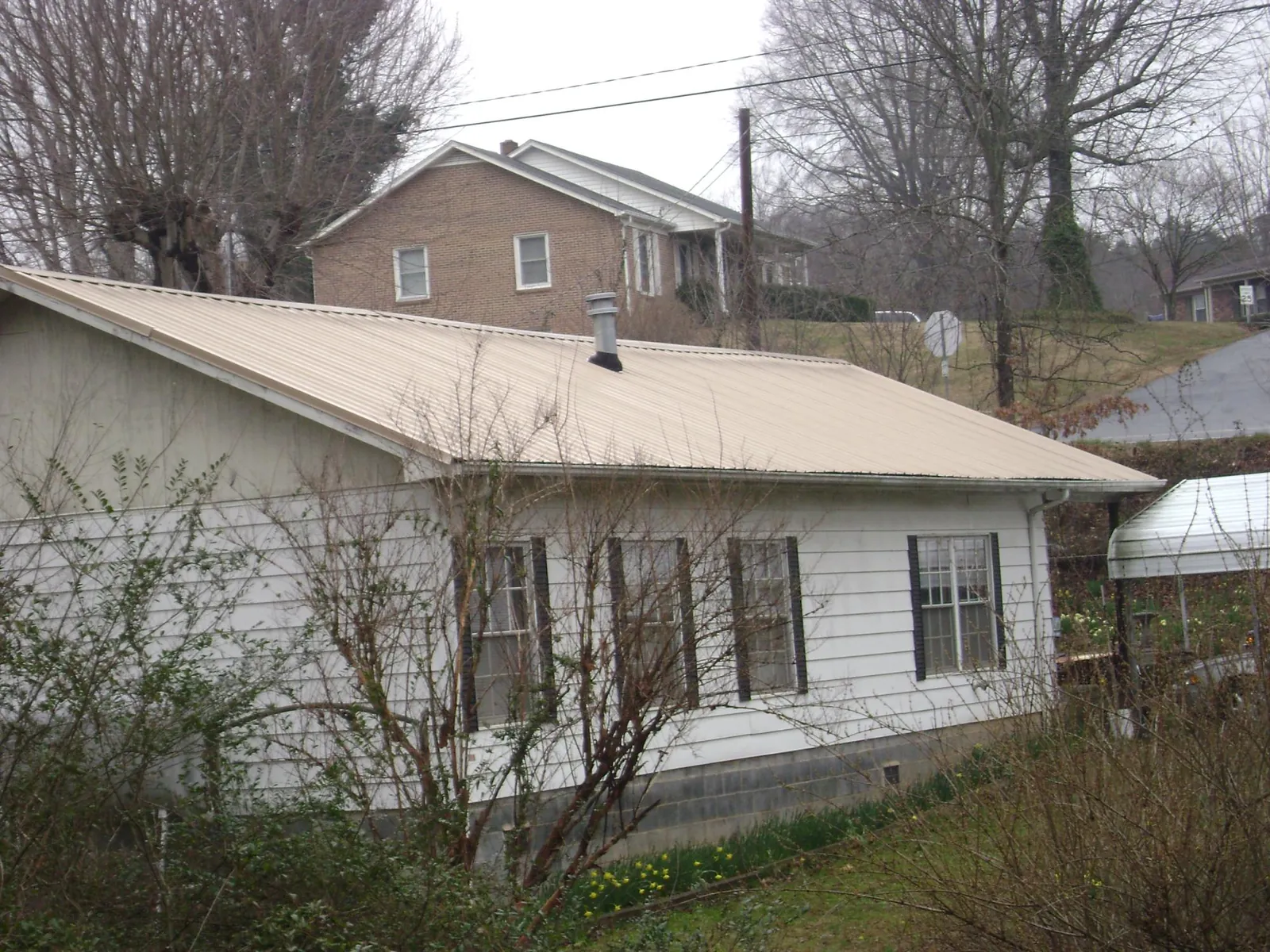 Tan metal roof on a white sided house set into a hillside — Commercial Roofing by Roofing Brothers in Highland Lakes