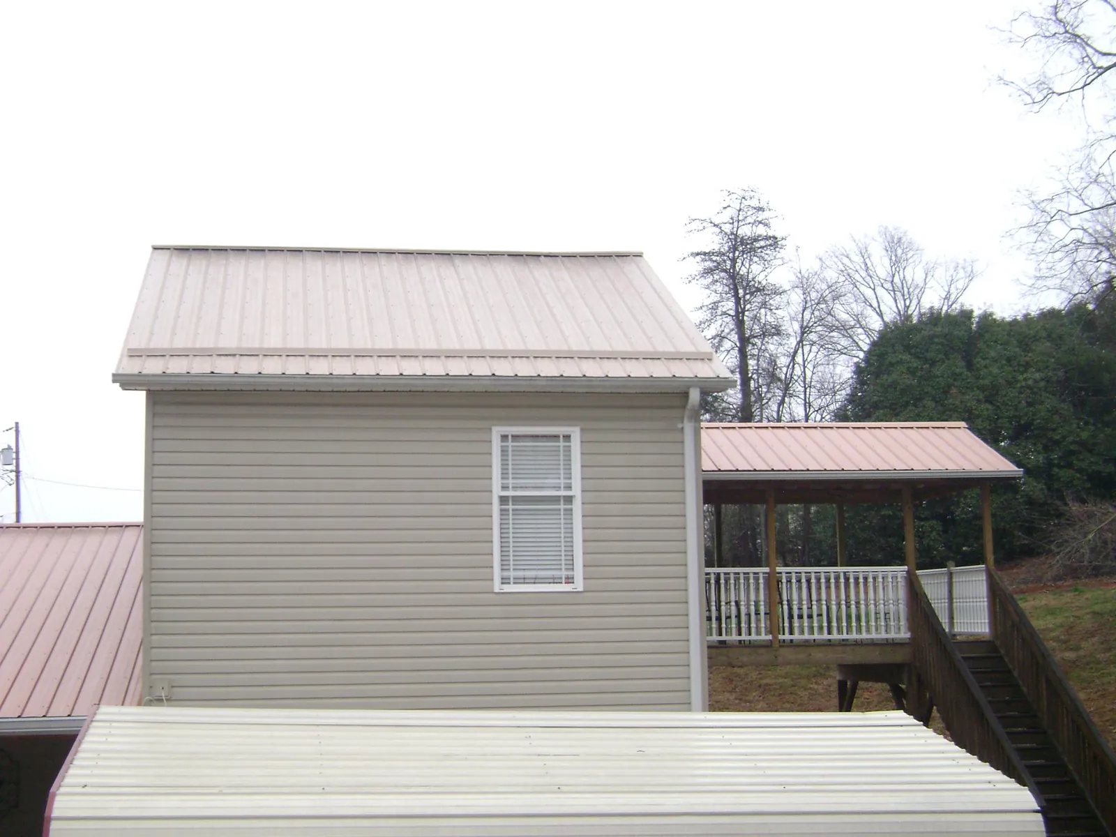 Tan metal roofs on a two story addition and attached porch, from a Roof Replacement job in Highland Lakes